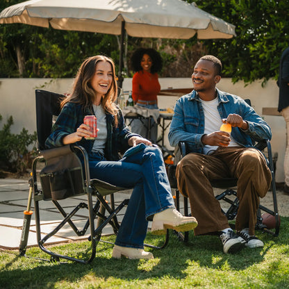 Two people having a drink in a backyard while sitting in a tailgater dark charcoal stowaway rocker. 
