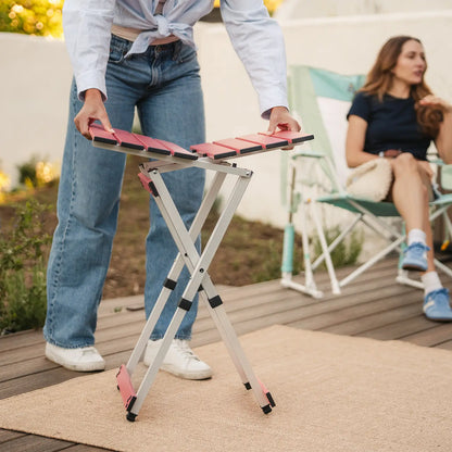 A woman assembling a coral Compact Camp Table near a group sitting in rockers. 