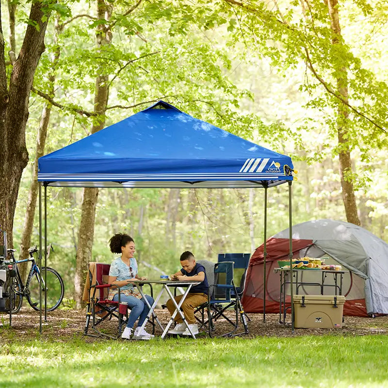 Two kids playing card games near a campsite while sitting under a Levrup Canopy. 