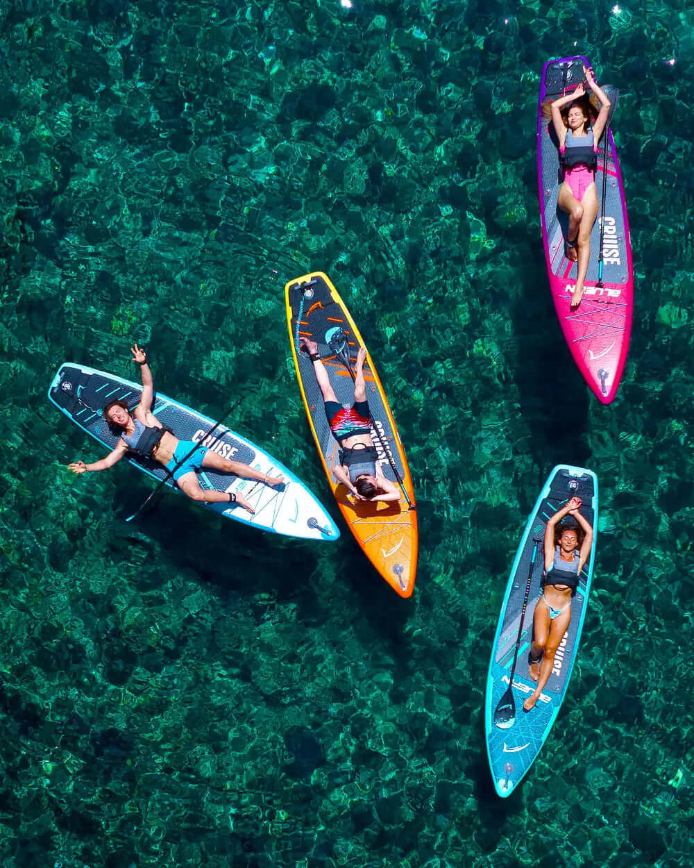 Four paddleboarders relaxing on colorful boards in clear water, showcasing vibrant designs and textures.