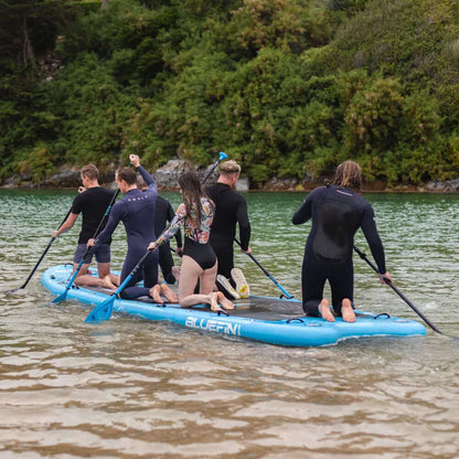 Group of six people paddling on a blue inflatable paddleboard in calm water