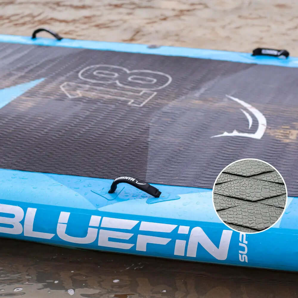 Inflatable paddleboard with textured deck pad, blue edges, and center fin on wet sand